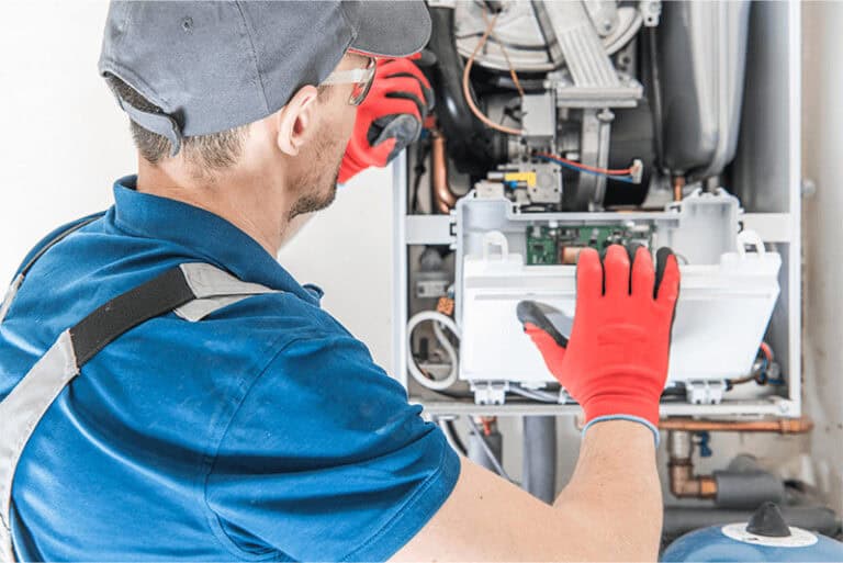 technician in blue examining inside of a gas furnace