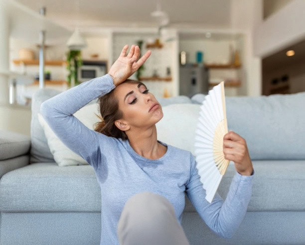 Woman with sweat stains on shirt fanning herself