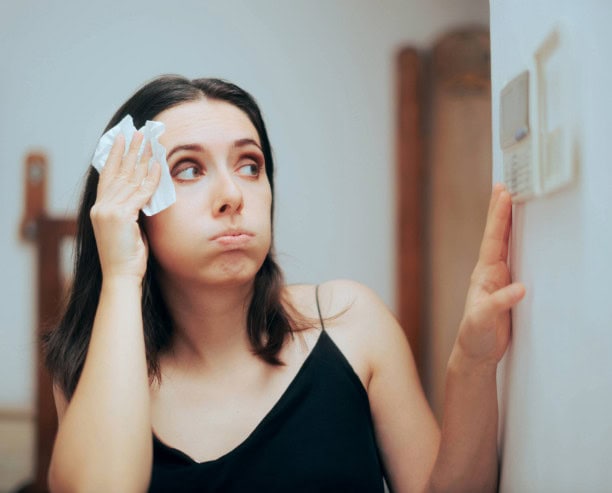 Woman wiping forehead while looking at thermostat